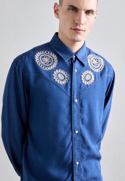 Denimhemd in tiefblau mit weißen gestickten Blumenmotiven auf den Schultern, Druckknöpfen und klassischem Kragen. Weiche Textur.