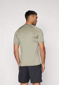 Kortermet idrettsgenser i lys olivengrønn, laget av stretchstoff. Inkluderer raglan-ermer og en subtil logo på baksiden av halslinjen.
