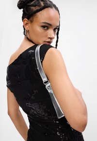 Melnas pērlīšu kleitas ar ziedu rakstu, bez plecu dizains. Modelis nēsā sudraba plecu somu. Gluda tekstūra, pieguloša silueta.