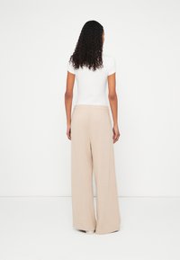 Béžové široké nohavice s textúrovaným vzhľadom a elastickým pásom, doplnené priliehavým bielym tričkom s krátkym rukávom, viditeľné zozadu.