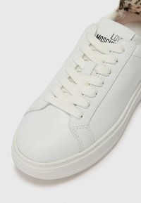 Baltos odinės sportbačiai su apvaliu pirštu, plokščiomis baltomis raištelėmis ir guminiais padais. Puikuojasi subtiliu siuvinėjimu ir ženklu ant liežuvėlio.