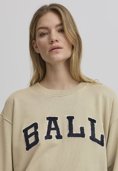Beige sweatshirt med ribbet halslinning og senkede skuldre. "BALL" i marineblå strukturbroderi på forsiden. Mykt, bomullsstoff.