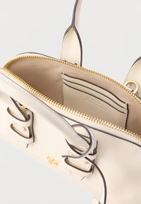 Kremfarvet læderhåndtaske med guldlynlås, indvendige kortholdere og sorte detaljer. Har dobbelthanke og knudedetalje på stropperne.