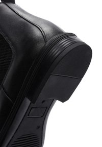 Zapato de cuero negro con parte superior texturizada, suela de goma y un diseño de tacón distintivo que presenta acentos acanalados y un área de botón de presión.