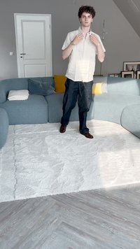 Tappeto chiaro e texture su un pavimento in legno; divano curvo blu con cuscini decorativi; outfit informale con jeans e scarpe.