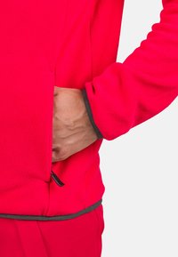 Fleece jacket in bright pink with a zippered pocket, gray accents at the cuffs and hem, featuring a soft texture and fitted design.