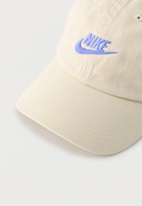 Μπεζ бейзбол καπέλο Nike με καμπυλωτό γείσο και κεντημένο μπλε λογότυπο Nike στο μπροστινό πάνελ, σε λευκό φόντο.