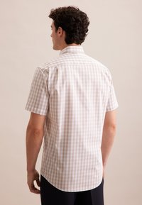 Camicetta a maniche corte a quadri in beige e bianco, con colletto classico e orlo curvo, realizzata in tessuto di cotone leggero.