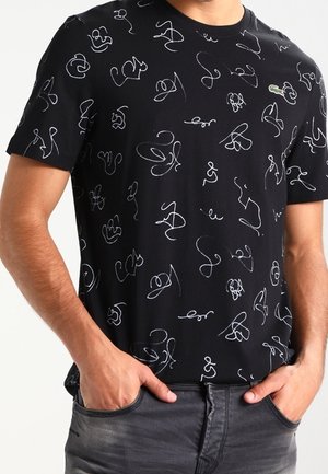 Schwarzes Kurzarmhemd mit abstrakten weißen Linienzeichnungen, getragen von einer Person mit den Händen in den Taschen dunkler grauer Jeans.