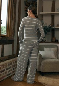 Set de haine de lounge cu dungi gri, care include un top cu mânecă lungă și pantaloni largi. Materialul pare moale și are o croială confortabilă. Accesoriile nu sunt incluse.