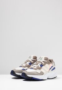 Grå och vita sportskor med blå accenter, i mocka och mesh, en tjock sula och tre-stripes branding på sidan.