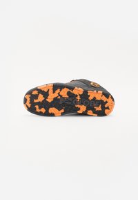 Black sneaker sole with orange camo pattern, featuring textured grip and logo detail. Durable rubber material with contrasting colors.