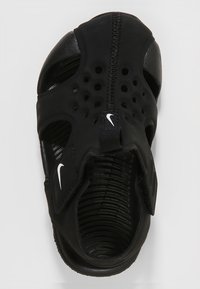 Svart atletisk sko med stängd tådesign, tillverkad av syntetiskt material med perforeringar och en texturerad sula, säkrad med ett band.