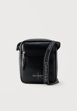 Sac bandoulière en cuir noir avec poche avant zippée et sangle ajustable de marque Calvin Klein.
