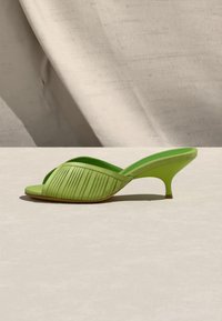 Πράσινο mule ανοιχτού δακτύλου με πλισέ επάνω μέρος και κοντό τακούνι kitten, τοποθετημένο σε λείο ανοιχτόχρωμο υπόστρωμα με ύφασμα στο φόντο.