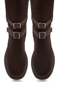 Botas marrones hasta la rodilla con correas de doble hebilla y parte superior texturizada, que presentan una puntera redonda y suave, y una suela gruesa y duradera.