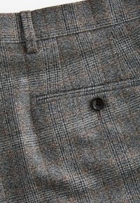 Gray plaid trousers with a textured fabric. Features a back pocket with a black button and brown accents in the check pattern.