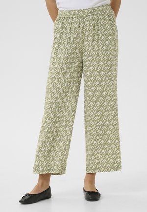 Jasnozielone spodnie o szerokich nogawkach z białym abstrakcyjnym wzorem liści, noszone z czarnymi balerinami i białą bluzką.
