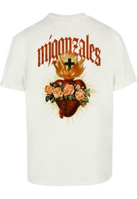Hvit bomull t-skjorte med et grafisk trykk av et brennende hjerte omgitt av roser, med ordet "migonzales" i fet rød skrift over.