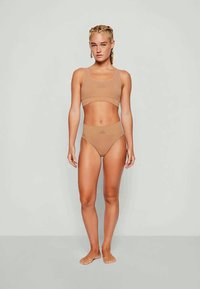 Kerge pruun sportlik rinnahoidja ja sobivad kõrge pihaotsaga aluspüksid, mis on valmistatud venivast kangast. Minimalistlik disain, sujuv tekstuur ja nähtamatud aksessuaarid.