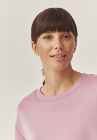 Lilla suderiga, millel on ümar kaelus ja lühikesed varrukad, valmistatud pehmest kangast. Sujuv tekstuur minimalistlikus disainis.