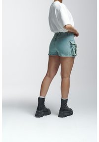 Shorts en denim bleu clair, avec poches cargo latérales. Associés à une chemise blanche ample et des bottes noires à lacets avec semelles épaisses.