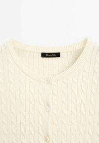 Kabelstrick-Cardigan in Cremefarbe mit rundem Ausschnitt, Knopfverschluss und strukturiertem Muster. Das Etikett ist im Kragen sichtbar.