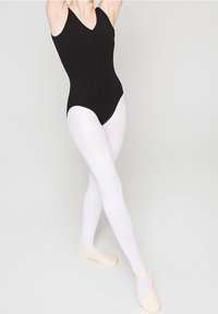 Persoon in een zwarte maillot, witte kousen en balletschoenen die in een gekruiste balletpositie staat tegen een effen achtergrond.