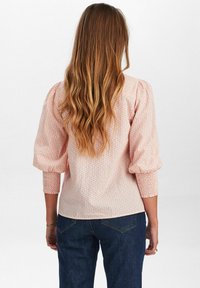 Blusa fucsia con motivo a fantasia, maniche a sbuffo e polsini arricciati, abbinata a jeans scuri. Tessuto morbido e delicato motivo floreale.
