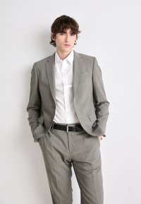 Completo grigio a scacchi con una vestibilità su misura, abbinato a una camicia bianca con bottoni. Cintura nera che accentua la vita. Design semplice e pulito.