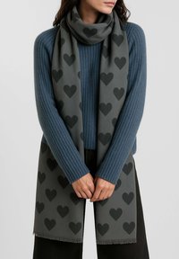 Sciarpa grigia con motivo a cuori ripetuti in grigio scuro, realizzata in materiale morbido, con bordi frangiati, drappeggiata intorno al collo.