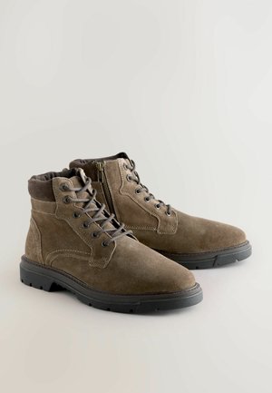Braune Wildleder-Stiefeletten mit Schnürung vorne, seitlichem Reißverschluss und Gummisohle. Mit gesteppten Details und gepolstertem Kragen.
