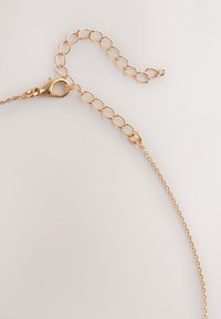 Gold chain necklace with adjustable link extension and lobster clasp on a light neutral background.