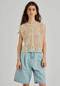 Gehaakt top in crème met hexagonale bloemenpatronen, met een ronde halslijn en korte mouwen, gecombineerd met losse denim shorts in lichtblauw.