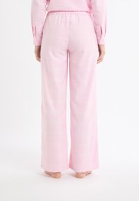 Pantaloni a gamba larga a quadri rosa con vita elastica e tessuto morbido. Il motivo presenta linee bianche a griglia su uno sfondo rosa chiaro.