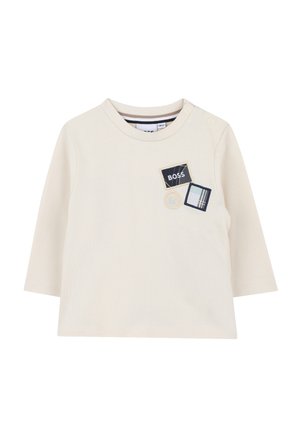 Cream-colored long-sleeve shirt featuring a round neck and three embroidered patches in navy, white, and beige with text and plaid designs.