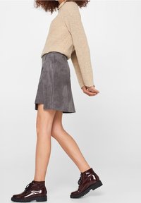 Beige gebreide trui, grijze suede flared rok en bordeauxrode patenten leren enkellaarzen met zwarte veters en dikke zolen.