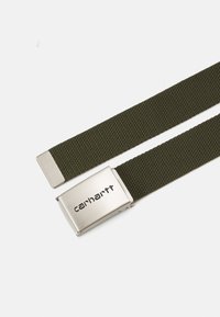 Cintura in tessuto intrecciato verde con una fibbia in metallo argentato che presenta il logo "Carhartt". La fibbia è rettangolare con bordi lisci.