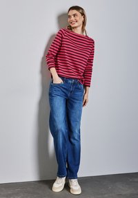 Roter und pink gestreifter Langarmoberteil kombiniert mit lockeren blauen Jeans und hellen Sneakers. Einfaches Design mit lässiger Passform.