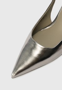 Metallic sølv spidse højhælede sko med en glat, skinnende overflade og en dyb udskæring i siderne, der afslører den polstrede inderside.