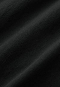 Schwarzer Baumwollstoff mit glatter Oberfläche, der subtile Falten und Knitter zeigt. Das Material wirkt leicht und hat eine einheitliche Farbe.