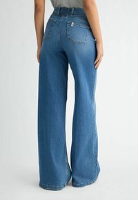 Jean en denim bleu à jambes larges avec une taille légèrement élastique, comportant deux poches arrière et une texture de tissu lisse.