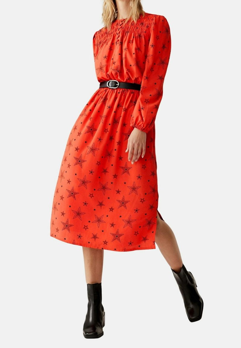 Röd midiklänning med svart stjärnmönster, gathered halsringning, lång ärm och elastisk midja, ihop med ett svart bälte och ankelboots.