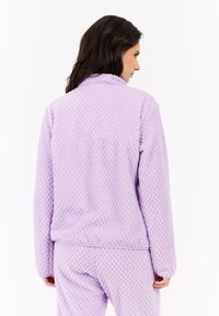 Fialová fleecová bunda s textúrovaným, nadýchaným dizajnom. Má vysoký golier a dlhé rukávy. Z pohľadu zozadu je vidieť voľný strih.