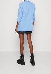 Light blue blazer with a structured design, three-quarter sleeves, and a back vent, paired with a black textured skirt and black boots.