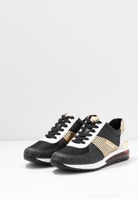 Black and white sneakers with gold accents, textured fabric, mesh panels; featuring a cushioned sole and lace-up design.
