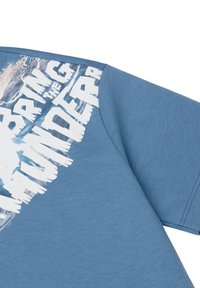 Blue cotton t-shirt featuring a graphic print in white with a rugged texture, positioned on the left shoulder, angled for display.