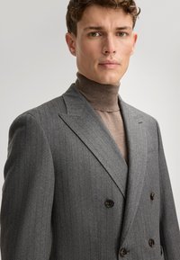 Blazer grigio a righe con design doppiopetto e bottoni neri. Abbinato a un dolcevita marrone chiaro. Dettaglio del tessuto strutturato visibile.