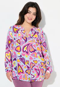 Blusa de manga larga en tejido azul claro con un colorido patrón de corazones en rosa, púrpura y amarillo. Cuello Henley y corte relajado.