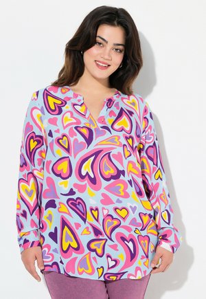 Blouse à manches longues en tissu bleu clair avec un motif de cœurs colorés en rose, violet et jaune. Encolure Henley et coupe décontractée.